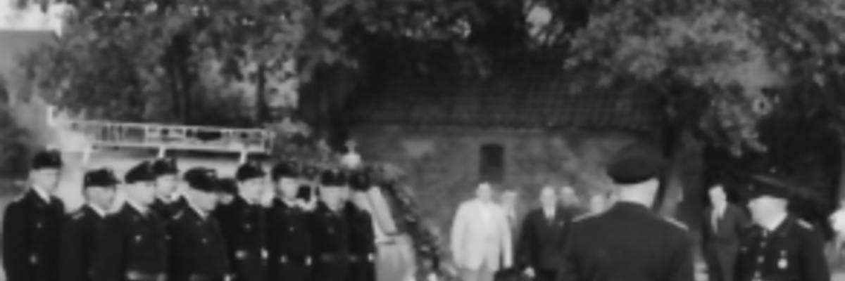 Vermutlich Parade der Feuerwehr, im Hintergrund Feuerwehrfahrzeug mit Leiter