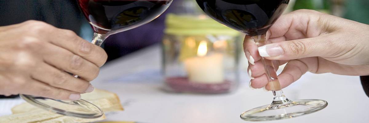 zuprostende Gläser mit Rotwein und Käseplatte im Vordergrund