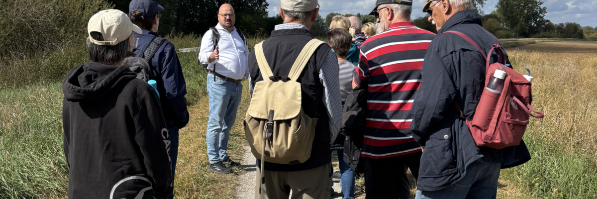 Bürgermeister Kai Eggert spricht auf einem Feldweg zu Personen, die Rucksäcke tragen.