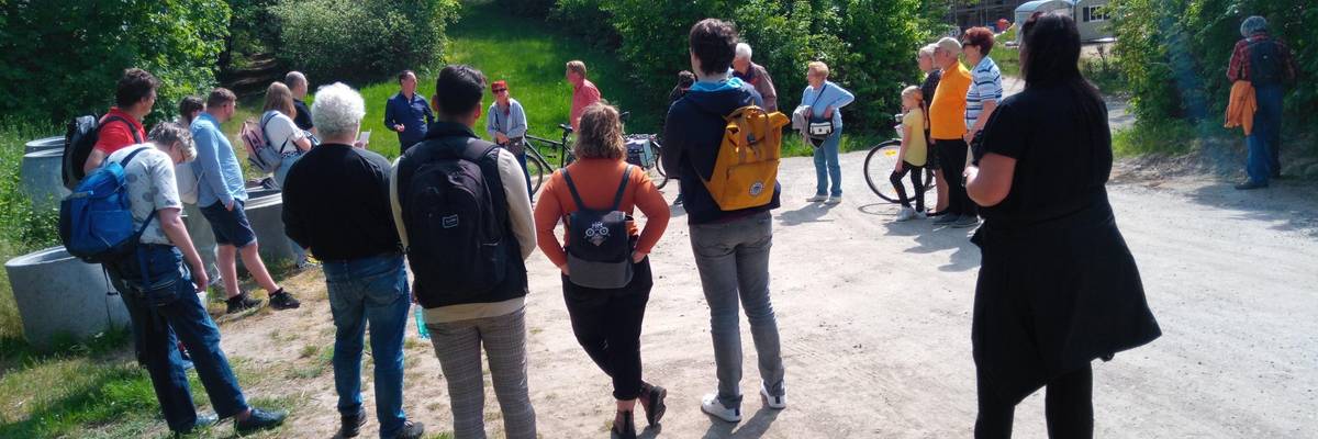 Eine Gruppe von Personen stehend im Kreis, die sich unterhalten. Im Hintergrund grüne Büsche und Gras.