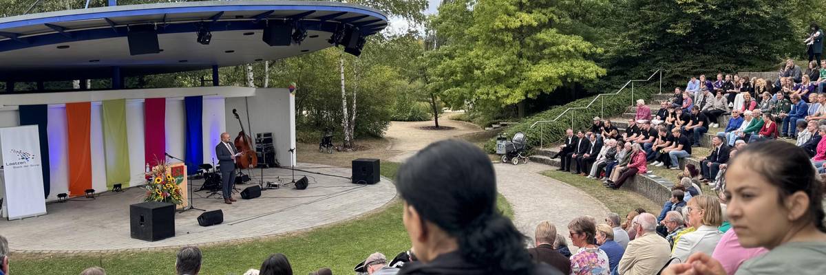 Blick auf die Kulturbühne im Park der Sinne. Bürgermeister Kai Eggert spricht. Viele Personen sitzen im Publikum.