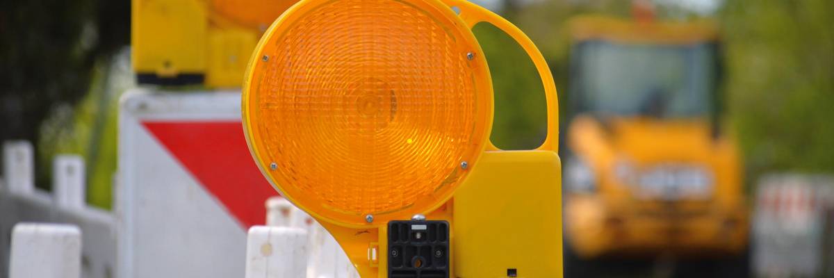 Straßenabsperrungen. Barken mit Signalleuchten. Im Hintergrund ist ein Bagger zu sehen.