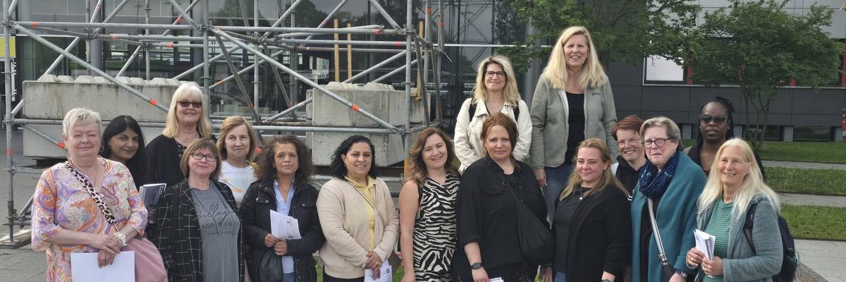 Die Teilnehmenden stehen vor dem Messeeingang. Es ist ein Gruppenbild. Sie stehen zusammen im Halbkreis.