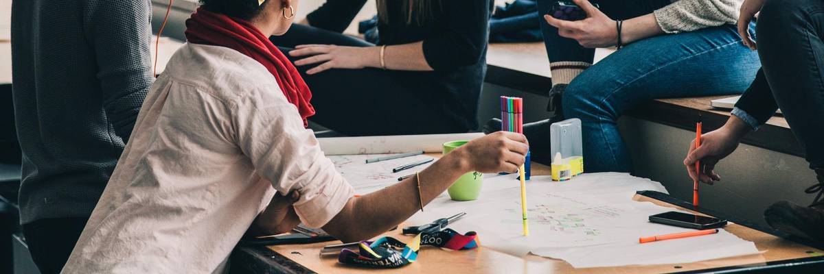 Jugendliche sitzen und stehen an einem Tisch mit Lernmaterialien