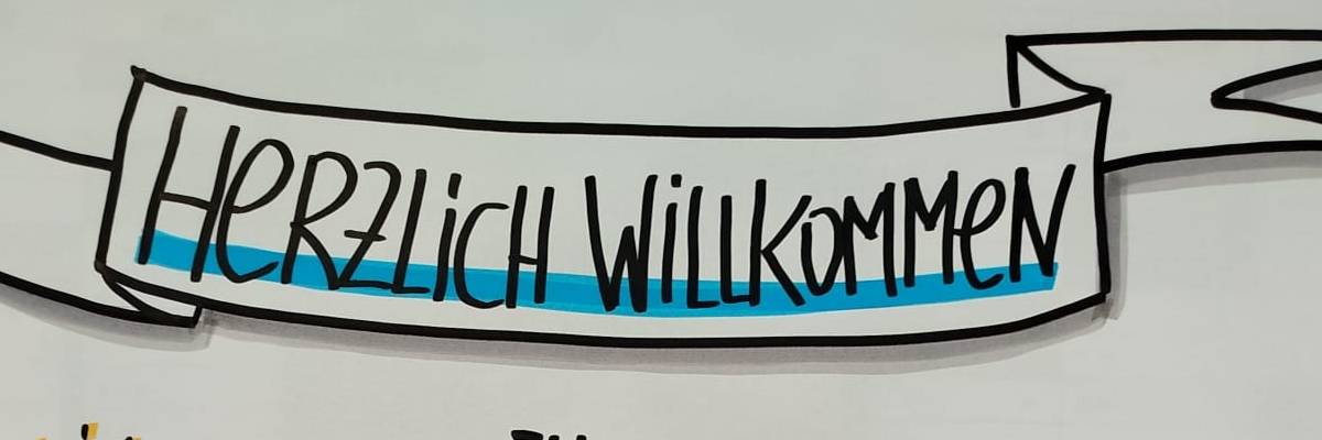 Auf einem Flipchartblatt steht "Herzlich willkommen zum Visual 2".