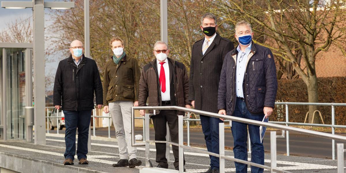 Fünf Männer stehen mit Masken auf einem Bahnsteig