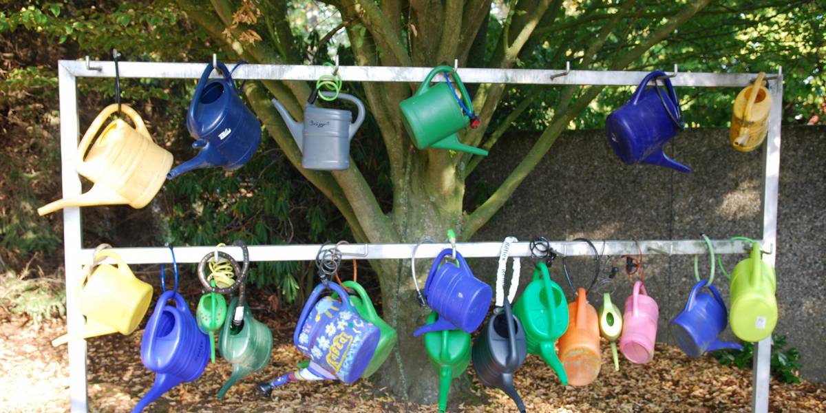 Bunte Gießkannen hängen an einem Metallgestell