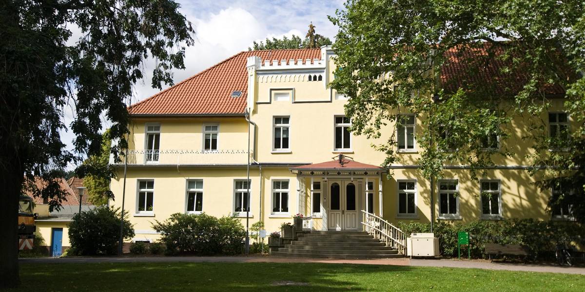 Gebäude steht in einem Park. Das Sonnenlicht strahlt das Gebäude an.