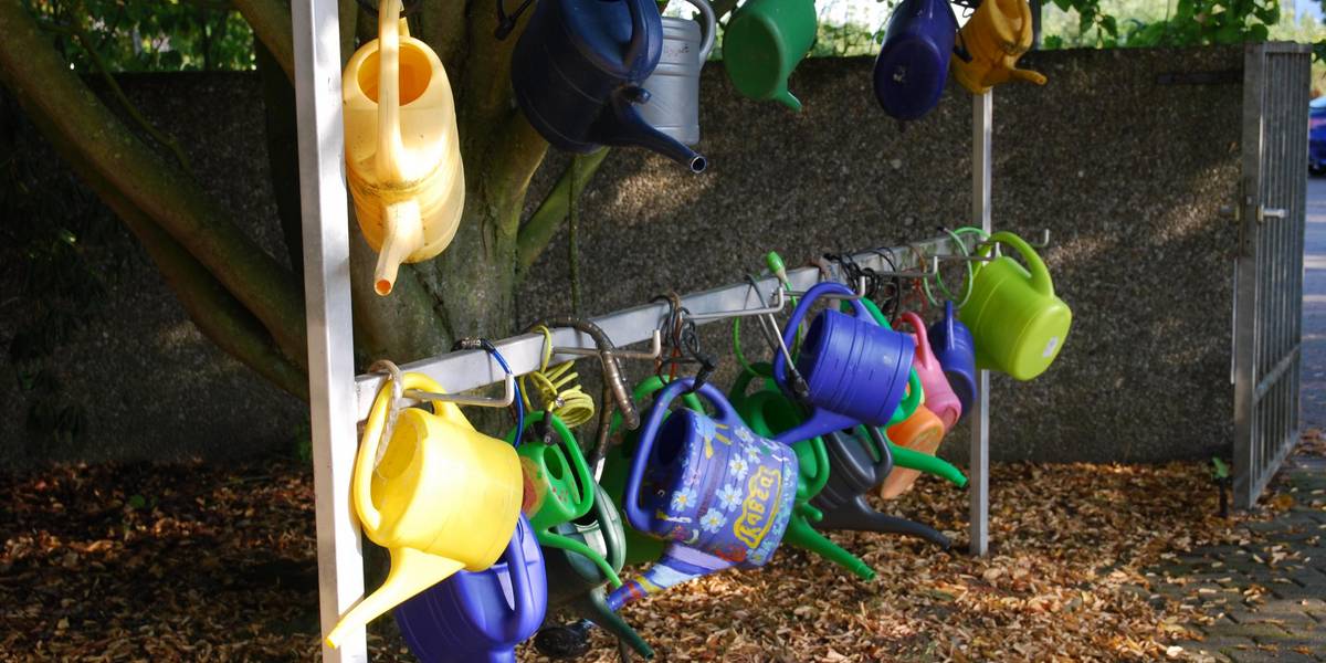Gießkannen auf dem Friedhof Rethen © Stadt Laatzen Bunte Gießkannen hängen an einem Metallgestänge.