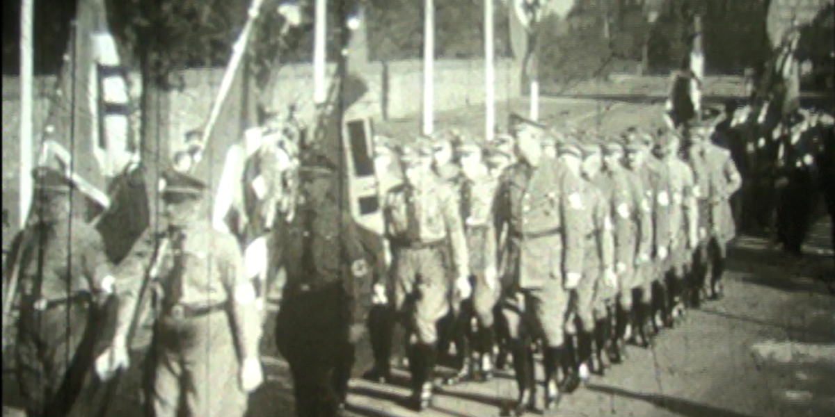 schwarz weiß Aufnahme von einer Reihe Männer in NS Uniformen, die marschieren.