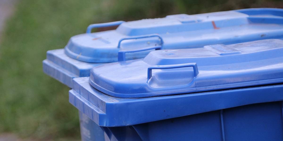 Zwei blauen Tonnen, von denen man nur die blauen Deckel sieht, stehen vor einer Wand.