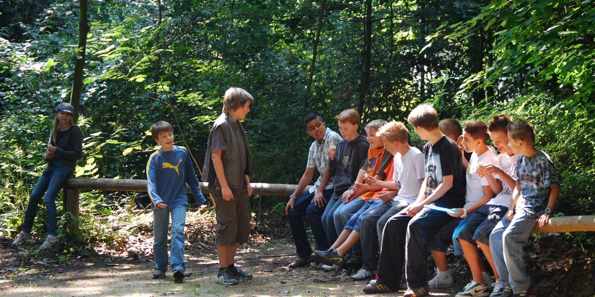 Eine Gruppe Jugendlicher sitzt im Wald auf einem Holzbalken