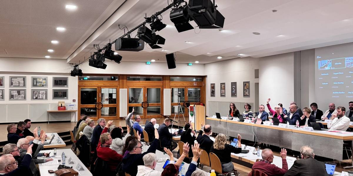 Menschen an Tischen heben die Hände zur Abstimmung.