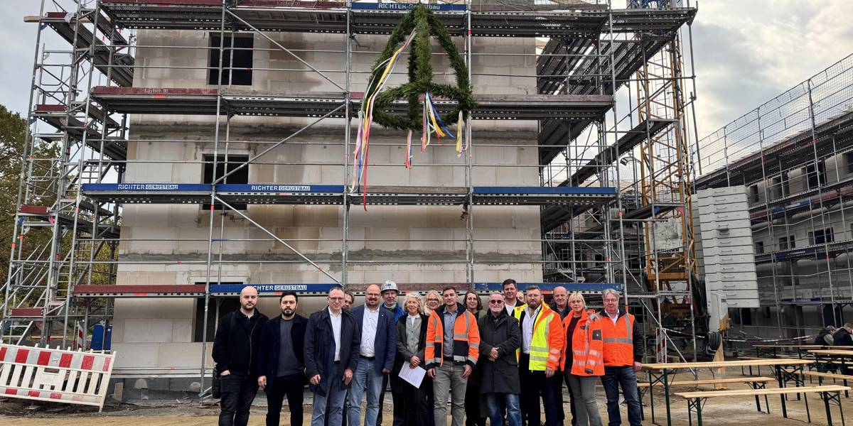 Richtfest an der Flüchtlingsunterkunft in Rethen: Am Nachmittag des 22. Oktobers kamen Bürgermeister Kai Eggert, Stadtrat Jörg Sporleder, Ortsbürgermeister Ernesto Nebot Pomar, die Teams Soziale Dienste und Hochbau der Stadt Laatzen, die Baufirma HTI-Bau sowie weitere Baubeteiligte zusammen, um den Meilenstein zu würdigen. © Stadt Laatzen Eine größere Gruppe Menschen stehen vor einem mehrstöckigen Rohbau, über ihnen hängt der Richtkranz an einem Kran.