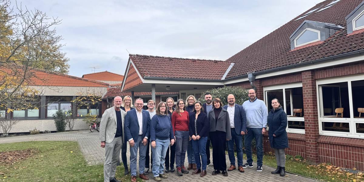 14 Personen stehen vor dem Eingang eines Schulgebäudes.