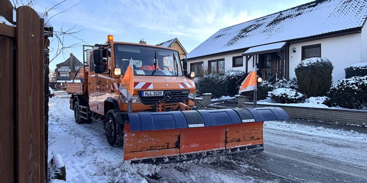 Ein Räumfahrzeug mit breitem Schneeschild fährt über eine verschneite Straße.