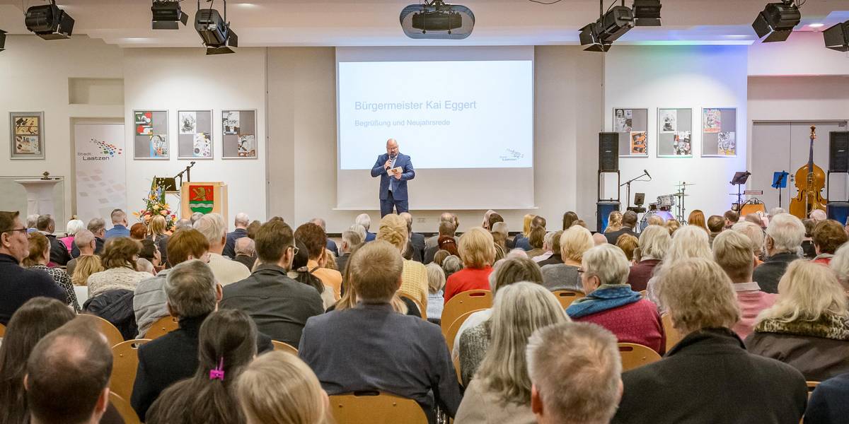 Neujahrsempfang im Forum der AES © Stadt Laatzen/Daniel Junker Blick über sitzende Menschen auf einen Redner an einem Rednerpult auf einer Bühne.
