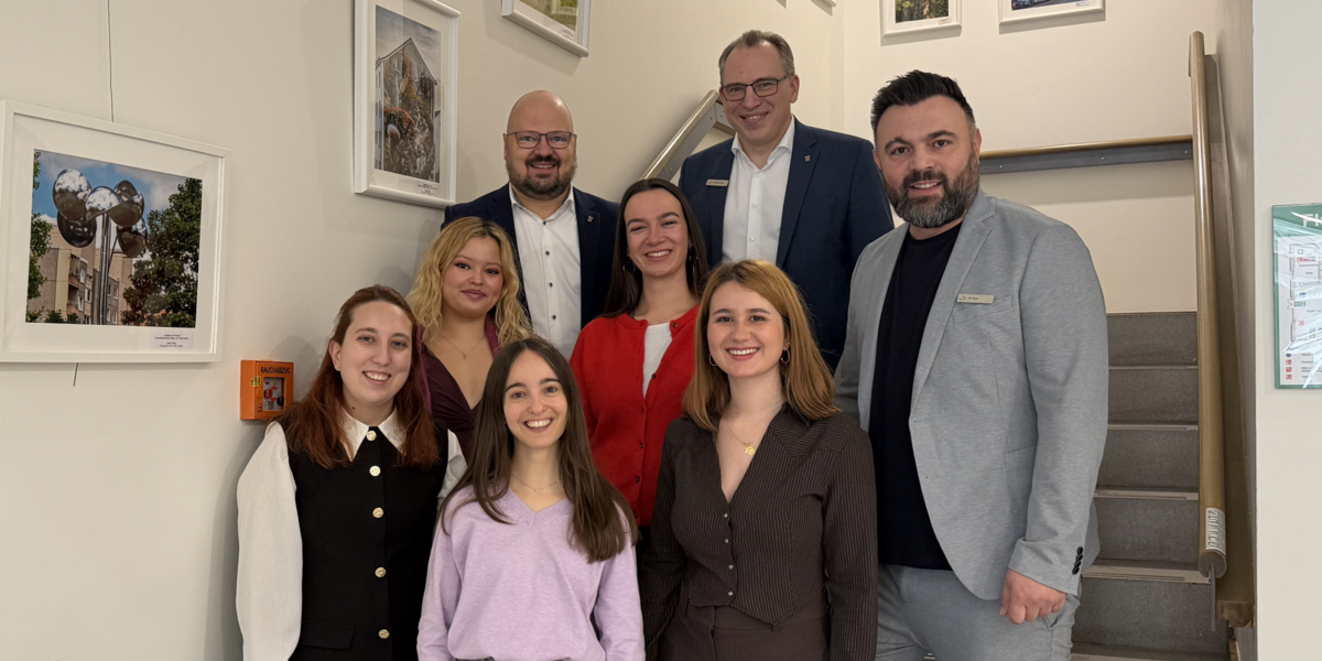 Fünf Frauen stehen neben drei Männern auf einer Treppe. Alle lächeln in die Kamera.