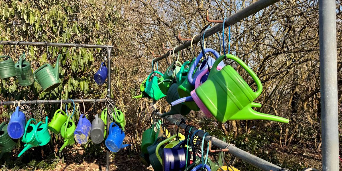 An einer Eisenstange sind bunte Gießkannen mit Schlössern befestigt.
