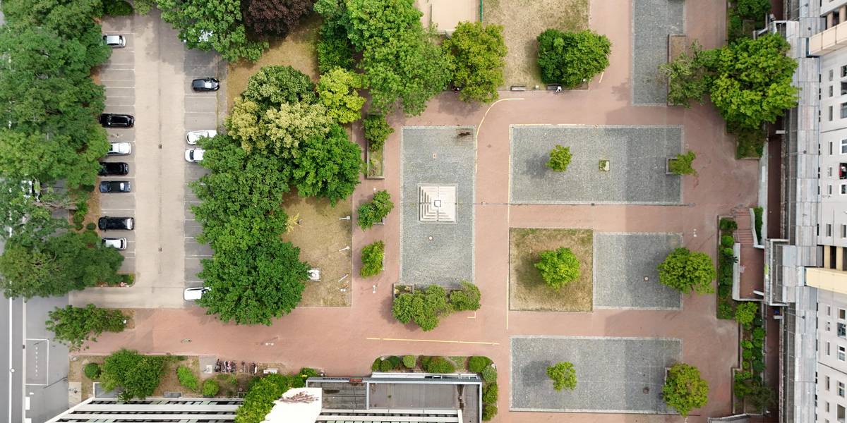 Ein Bild des Marktplatztes von oben. Man sieht den Brunnen, die Grünflächen und eine Fußballfläche.