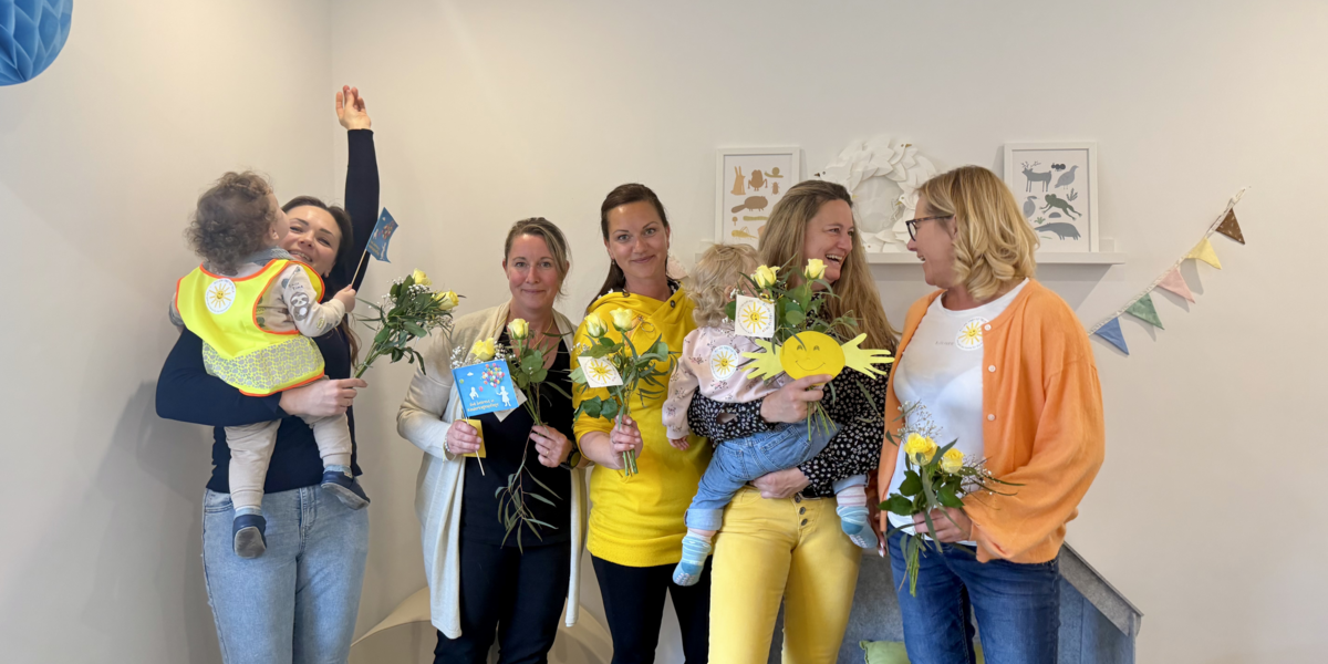 Fünf Frauen stehen gut gelaunt nebeneinander. Zwei von ihnen haben ein Kleinkind auf dem Arm.