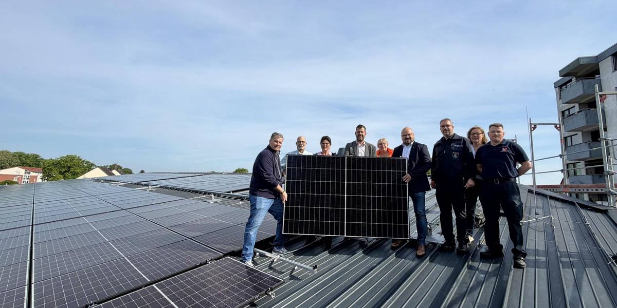 Eine Gruppe steht auf einer Dachfläche mit zahlreichen PV-Modulen und hält ein Solarpaneel in die Kamera.