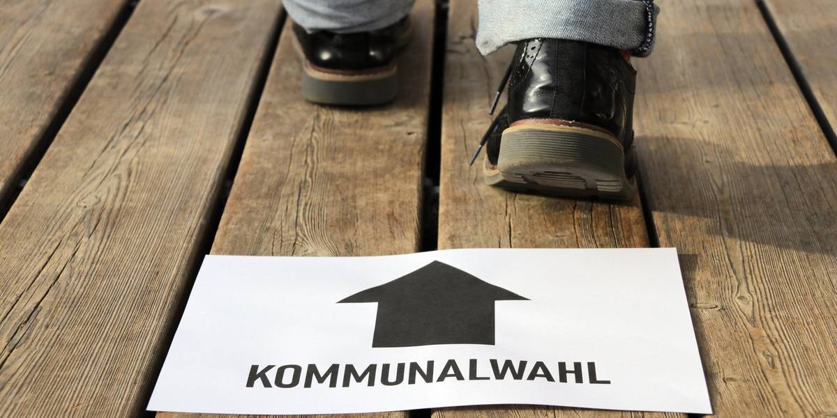 Ein weißes Blatt Papier mit der Aufschrift Kommunalwahl und Füsse, die dahinter stehen.
