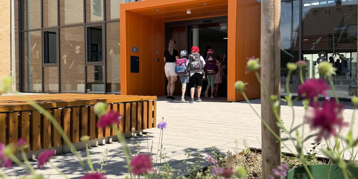 Am Tag der Eröffnungsfeier besichtigen die Schülerinnen und Schüler erstmals ihre neue Schule. Der Unterricht startet zum Schuljahresbeginn 2026/2027 im Neubau. © Stadt Laatzen Kinder mit Schulranzen gehen durch eine gläserne Schiebetür.