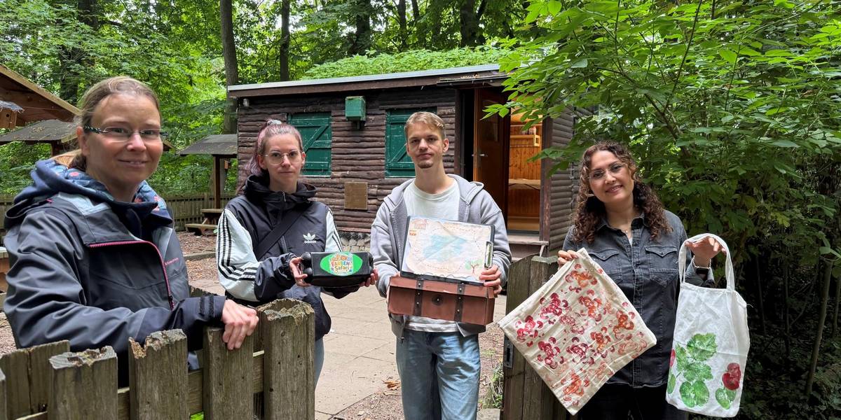 Mit viel Engagement und Kreativität haben Sarah Barfigo (2. v. r., Kita Sehlwiese), Lukas Nonnemann (Kita Marktplatz) und Zahra Tohidtabar (Kita Wülferoder Straße) ein abwechs-lungsreiches Programm für die Vorschulkinder an der Maria-Troll-Hütte in der Leinemasch entwickelt. Kita-Ausbildungsleiterin Susanne Grothe (l.) machte sich vor Ort ein Bild von den Ideen der angehenden Erzieherinnen und Erzieher. © Stadt Laatzen Drei Frauen und ein Mann stehen an einer Hütte im Wald und halten verschiedene Bastelwerke in die Kamera