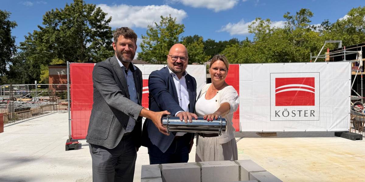 Eine Kapsel voller Erinnerungen und Zukunftspläne: Bürgermeister Kai Eggert (mittig) legt gemeinsam mit Stadtrat Hauke Schröder und Anja Chrobock, Schulleiterin der Grundschule Im Langen Feld, die Zeitkapsel in den Grundstein des Schulneubaus. © Stadt Laatzen Zwei Männer und eine Frau halten eine silberne Kapsel über eine Öffnung aus Mauersteinen.