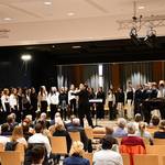 Schülerinnen und Schüler in schwarzer, weißer oder schwarz-weißer Kleidung stehen auf der Bühne und singen.