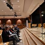 Seitlicher Blick auf Bühne und Publikum. Ein Mann im Anzug hält eine Rede.