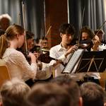 Zahlreiche Menschen mit Streichinstrumenten sitzen hinter Notenständern.