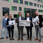 Vier Männer und eine Frau stehen vor der grauen Klinkerfassade eines neuen Schulgebäudes und halten gemeinsam zwei überdimensionierte Schlüssel.