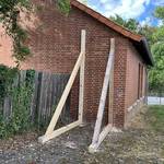 Ein Kantholz stützt die Rückseite eines roten Backsteingebäudes.