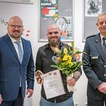 Verleihung des Couragepreise © Stadt Laatzen/Daniel Junker Drei Männer stehen in einer Reihe. Der Männ in der Mitte hält eine Urkunde und einen Blumenstrauß.