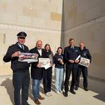 Bürgermeister Kai Eggert und Mitglieder der Feuerwehr stehen in einer Reihe und halten verschiedene Gegenstände in die Kamera u.a. die Tageszeitung und die Baupläne.