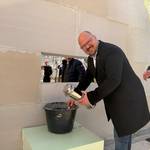 Bürgermeister Kai Eggert beugt sich über einen Eimer mit Mörtel und hält die silbere Zeitkapsel.