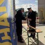 Zwei Männer in Feuerwehruniform befüllen gemeinsam eine Zeitkapsel.