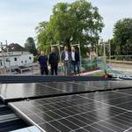 Dachfläche mit Solarmodulen und im Hintergrund stehen vier Personen auf einem Gerüst