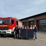 Eine Gruppe Menschen hält ein Solarmodul, neben ihnen steht ein Löschfahrzeug der Freiwilligen Feuerwehr.
