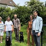 Eine Gruppe von Frauen, Männern und Hunden auf einer eingezäunten Wiese.