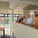 Mit Blick in die lichtdurchflutete Pausenhalle der neuen Grundschule Ingeln-Oesselse: Bildungs-Fachbereichsleiter Ali Kara (von vorne), Stadtrat Jörg Sporleder, Schulleiter Tobias Ahlswehde, Bürgermeister Kai Eggert und Stadtrat Hauke Schröder freuen sich, dass der Neubau nach dreijähriger Bauzeit bezugsbereit ist. © Stadt Laatzen Fünf Männer stehen an einer Mauer und blicken über eine moderne Pausenhalle