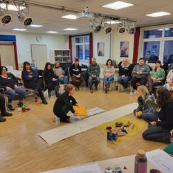 Teilnehmende sitzen in einem Stuhlkreis und hören den Referentinnen zu.