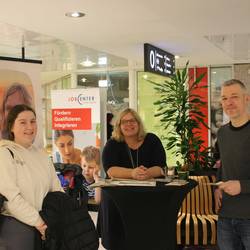 Am Stand von Uschi Drude informiert sich eine FSJ-lerin mit ihrem Anleiter aus der Kita. Sie tauschen sich an einem Stehtisch aus.