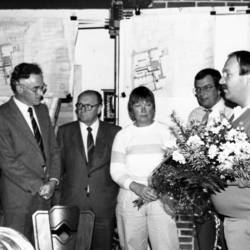 Sechs Personen, einige von ihnen mit Blumensträußen, im Hintergrund Karten an der Wand.