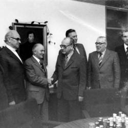 Gruppenfoto von 7 Herren, vorne stehen Flaschen auf dem Tisch, hinten ein Gemälde eines Mannes an der Wand.