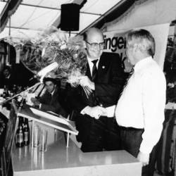 Übergabe eines Blumenstraußes an einen Herrn vor einem Rednerpult in einem Festzelt.