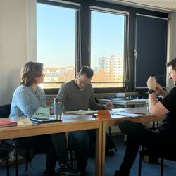 Drei Teilnehmende sitzen am Tisch und bearbeiten ein Arbeitsblatt.