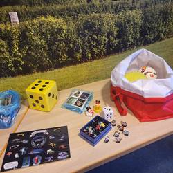Es stehen auf einem Tisch Materialien zur Verfügung. Würfel, Aufkleber, Badeenten, Ottifanten,...